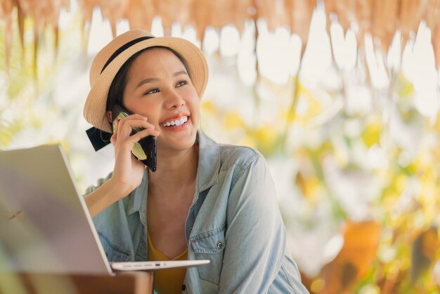 Trabajo y vacaciones mujer asiática nómada digital estilo de vida milenario mano sostener conversación de teléfono inteligente con el cliente en el extranjero reunión a distanciamujer asiática ropa casual caminando hablando en la playa océano