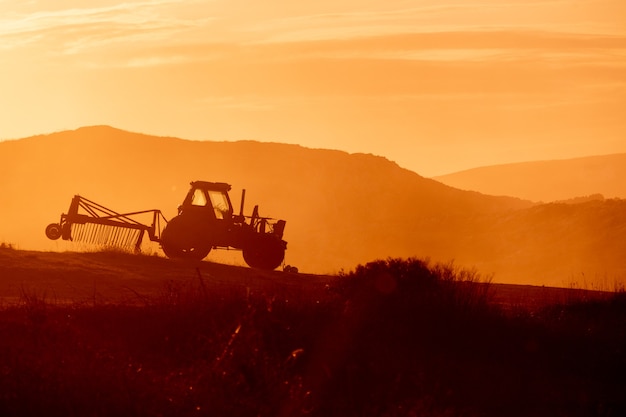 Tractor en un campo agrícola al atardecer. Tonos cálidos de luz de fondo