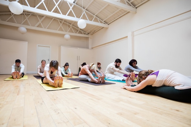 Trainer grupo de personas ayudando con el ejercicio pashimottanasana