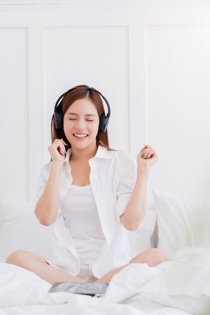 Traje de vestido blanco de mujer asiática de felicidad disfrutar de bailar escuchando música con fondo de dormitorio de auriculares