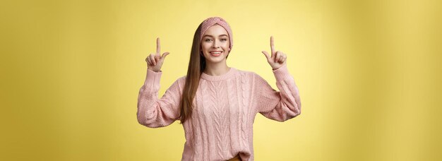 Foto gratuita tranquila hermosa joven estudiante en diadema de suéter de punto apuntando hacia arriba promocionando publicidad