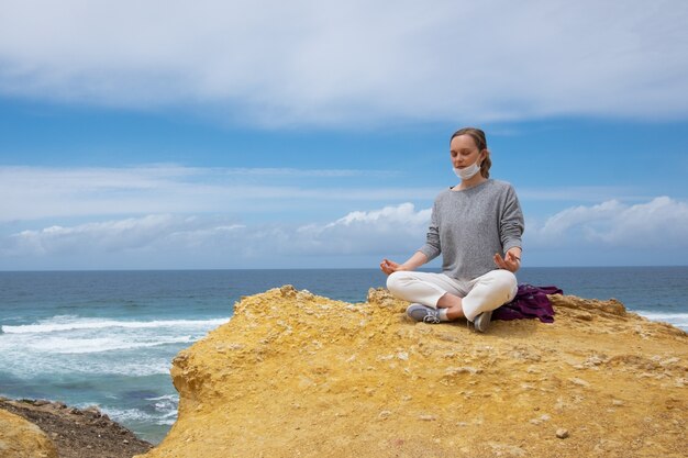 Tranquila joven en mascarilla meditando en el océano