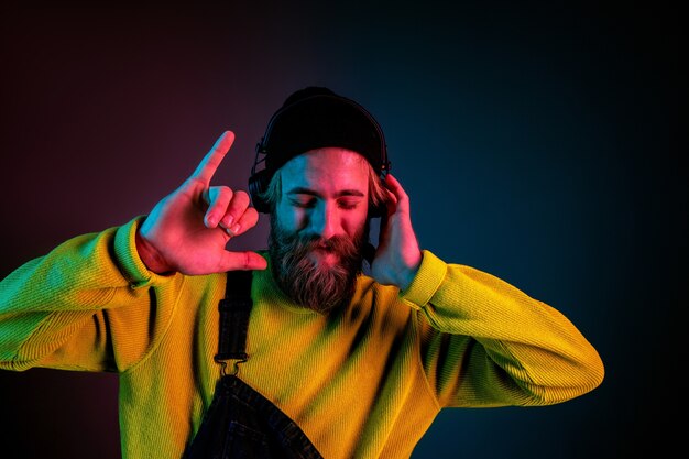 Tranquilo, feliz. Retrato de hombre caucásico sobre fondo de estudio degradado en luz de neón. Hermoso modelo masculino con estilo hipster en auriculares. Concepto de emociones humanas, expresión facial, ventas, publicidad.