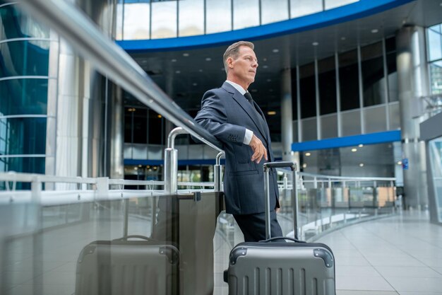 Tranquilo hombre de negocios pensativo con la maleta parada en la terminal del aeropuerto