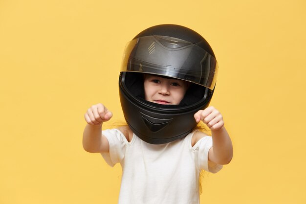 Transporte, extremo, deportes de motor y concepto de actividad. Retrato de niña peligrosa jinete en casco de motocicleta protector negro manteniendo las manos delante de ella como si condujera una motocicleta