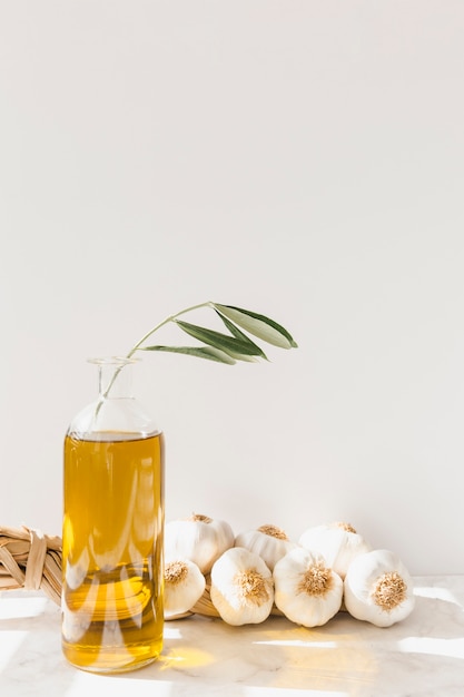 Trenza de bulbo de ajo con botella de aceite de oliva contra la pared blanca