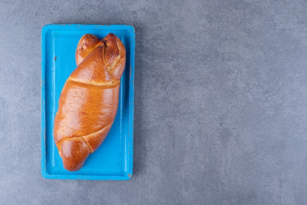 Trenza de pan dulce en una placa de madera sobre mesa de mármol.