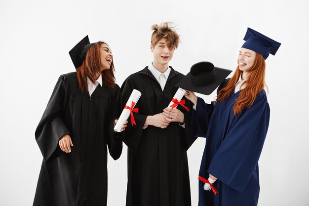 Tres alegres graduados sonrientes hablando tontos sosteniendo diplomas intimidación y burlarse