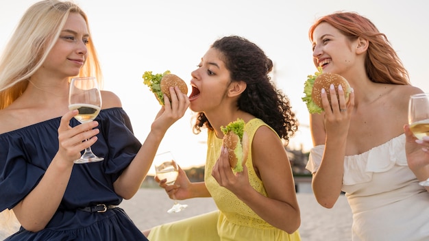 Foto gratuita tres amigas comiendo hamburguesas juntas en la playa