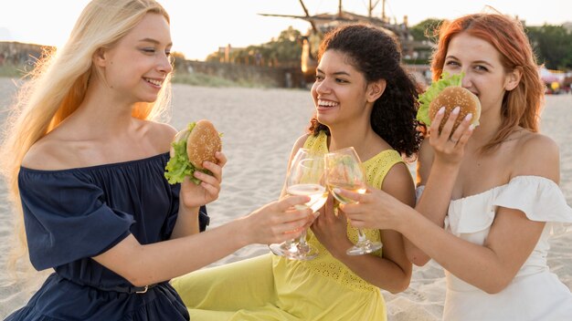 Tres amigas comiendo hamburguesas en la playa juntos