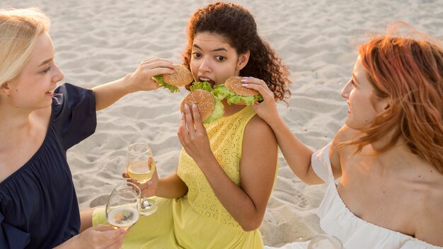 Tres amigas comiendo hamburguesas en la playa.