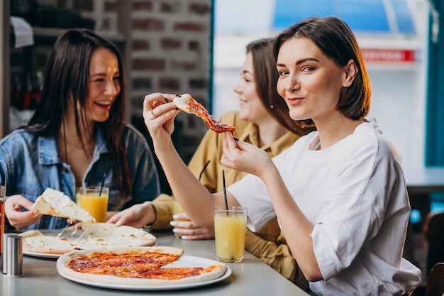 Tres amigas comiendo pizza en un bar