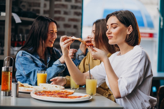 Tres amigas comiendo pizza en un bar