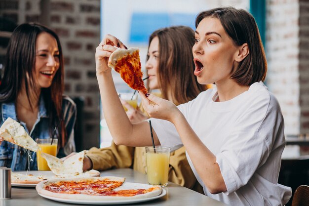 Tres amigas comiendo pizza en un bar