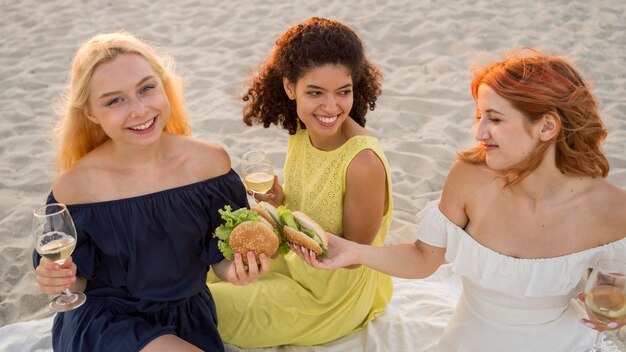 Tres amigas felices disfrutando de hamburguesas juntos en la playa