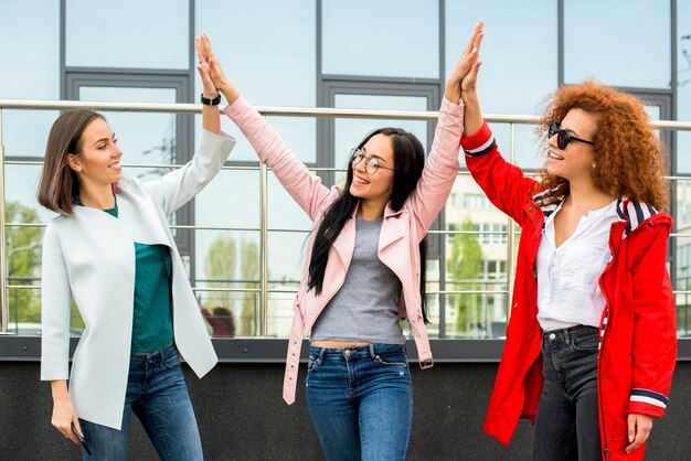 Tres amigas de moda dando alta cinco al aire libre