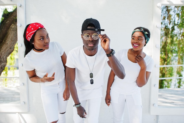 Tres amigos afroamericanos elegantes y de moda visten ropa blanca contra espejos Moda callejera de jóvenes negros Hombre negro con dos niñas africanas