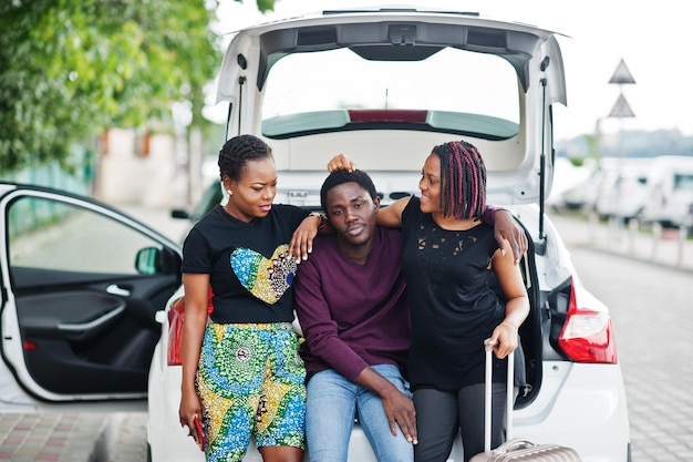 Tres amigos afroamericanos se sientan en el maletero del coche.