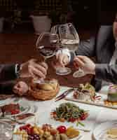 Foto gratuita tres amigos animan copas de vino con vino tinto y blanco en la cena