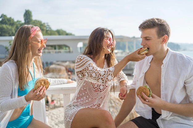 Tres amigos comiendo hamburguesas en la playa juntos