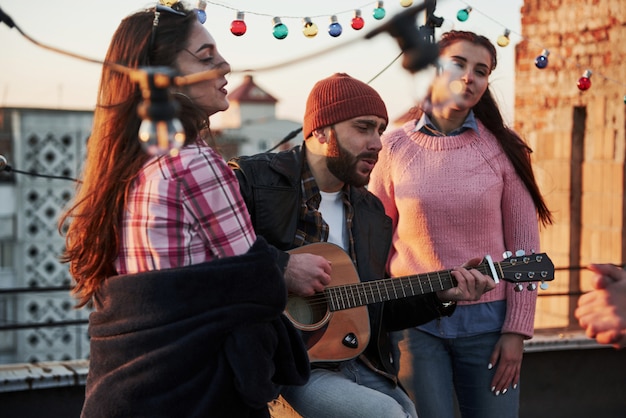 Tres amigos disfrutan cantando canciones de guitarra acústica en la azotea