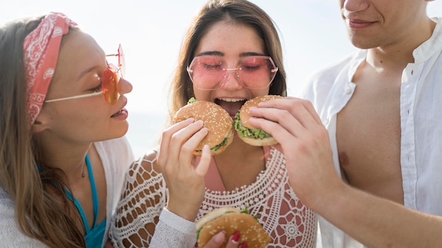 Tres amigos felices comiendo hamburguesas juntos al aire libre