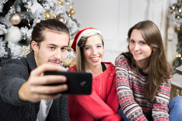 Tres amigos haciendo selfie enfrente de árbol de navidad