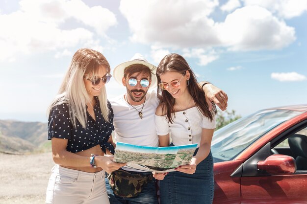 Tres amigos mirando el mapa de pie cerca del coche al aire libre