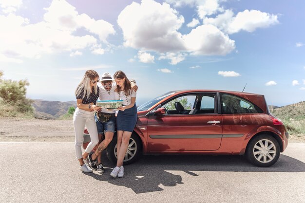 Tres amigos que miran el mapa que se coloca cerca del coche moderno en el camino
