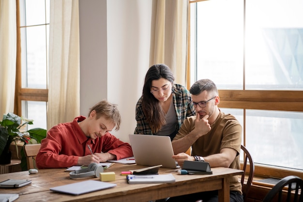 Tres amigos que usan libros y una computadora portátil para estudiar en una biblioteca