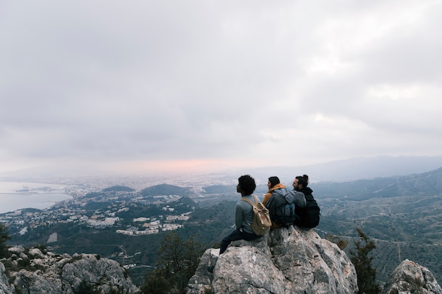 Tres amigos sentados en la cima de la montaña disfrutando de la vista panorámica