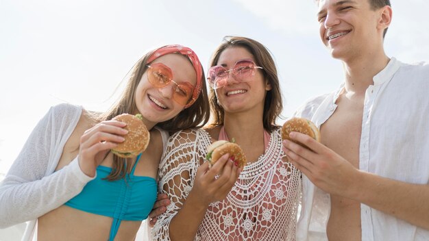 Tres amigos sonrientes al aire libre comiendo hamburguesas juntos