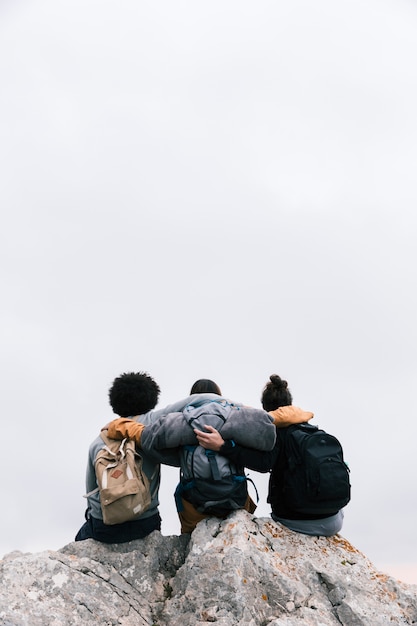 Tres amigos con sus brazos alrededor sentados en la cima de la montaña