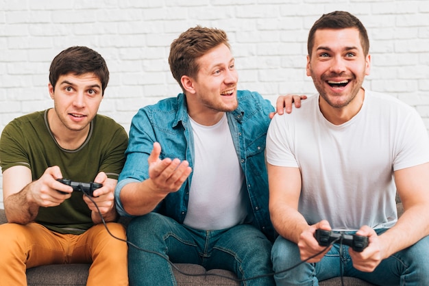 Tres amigos varones sentados juntos disfrutando el videojuego