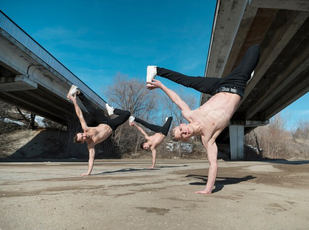 Tres artistas de hip hop sin camisa que practican la rutina de baile afuera