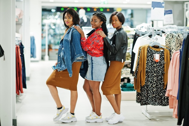 Tres atractivas mujeres afroamericanas vestidas con túnica marrón posadas en la tienda de ropa Es hora de ir de compras