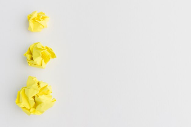 Tres bolas de papel arrugado amarillo de diferentes tamaños contra el fondo blanco.