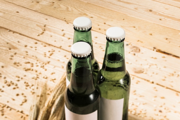 Foto gratuita tres botellas alcohólicas verdes y espigas de trigo en un tablón de madera