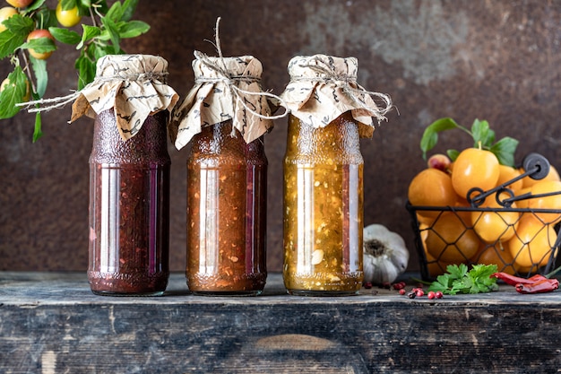 Tres botellas de vidrio de salsa tkemali georgiana variada con ingredientes sobre la mesa de madera rústica