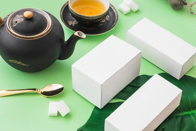 Foto gratuita tres cajas blancas con té de hierbas y cubos de azúcar sobre fondo verde