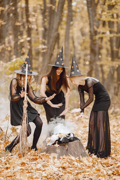 Tres chicas brujas en el bosque en Halloween. Chicas con vestidos negros y sombreros de cono. Las brujas hacen una poción mágica.