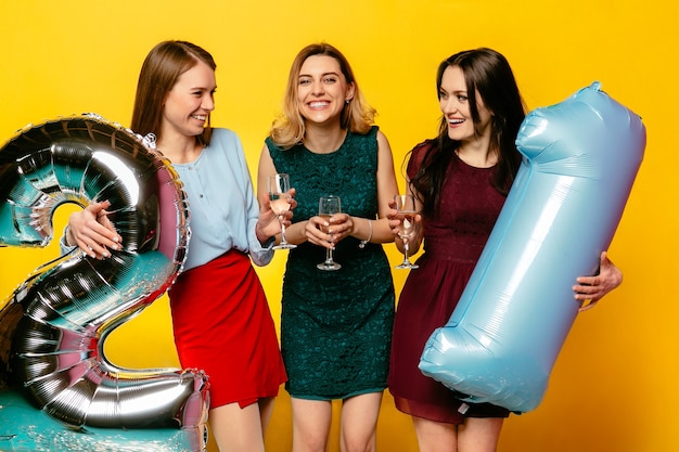 Foto gratuita tres chicas elegantes vistiendo vestidos, bebiendo champán, divirtiéndose