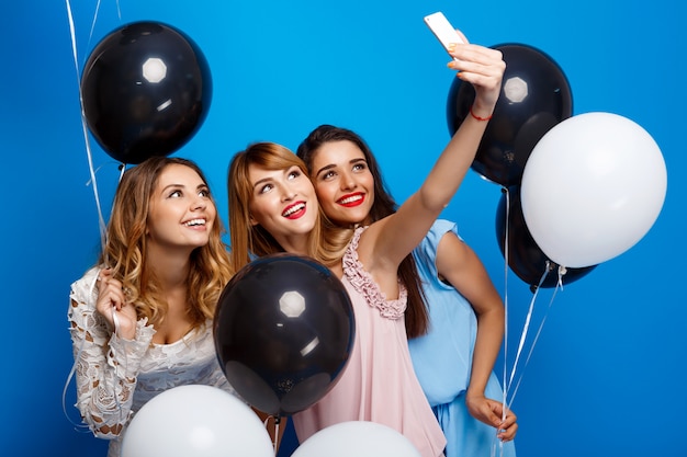 Tres chicas guapas haciendo selfie en fiesta sobre pared azul