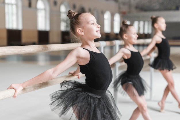 Foto gratuita tres chicas posando con ayuda de barre en estudio de danza