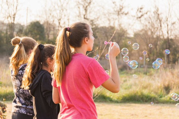 Tres chicas soplando burbujas con varita en el parque