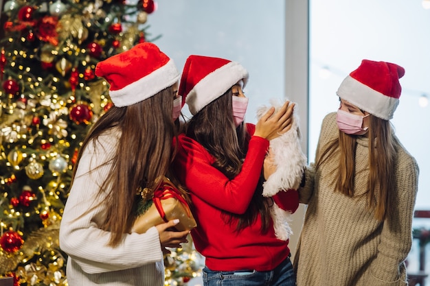 Tres chicas y un terrier posando para la cámara en la víspera de año nuevo. Navidad durante el coronavirus, concepto