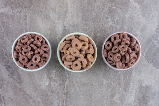 Tres coloridos cuencos de anillos de cereal de chocolate para el desayuno.