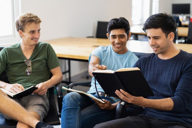 Tres compañeros estudiando, leyendo libros de texto y hablando