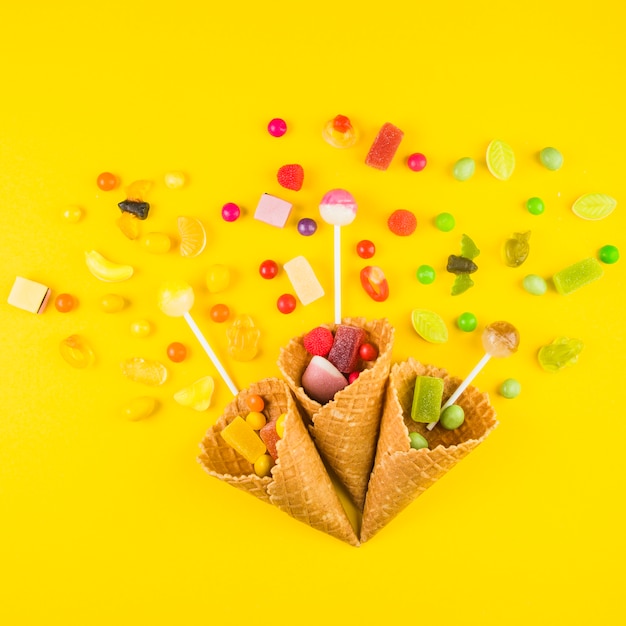 Foto gratuita tres conos de gofres de helado con variedades de dulces sobre fondo amarillo