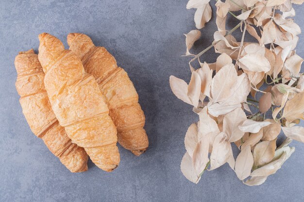 Tres croissant francés clásico con hojas decorativas sobre fondo gris.